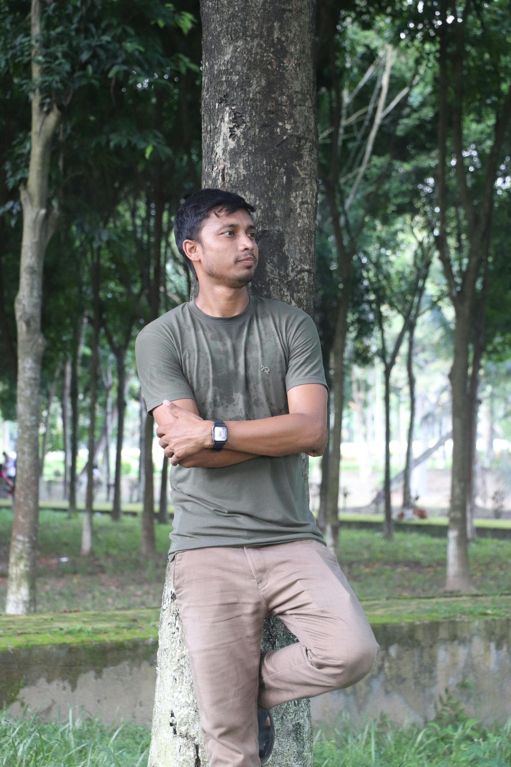Casual portrait of a man leaning on a tree in a lush green park in Rangpur, Bangladesh.