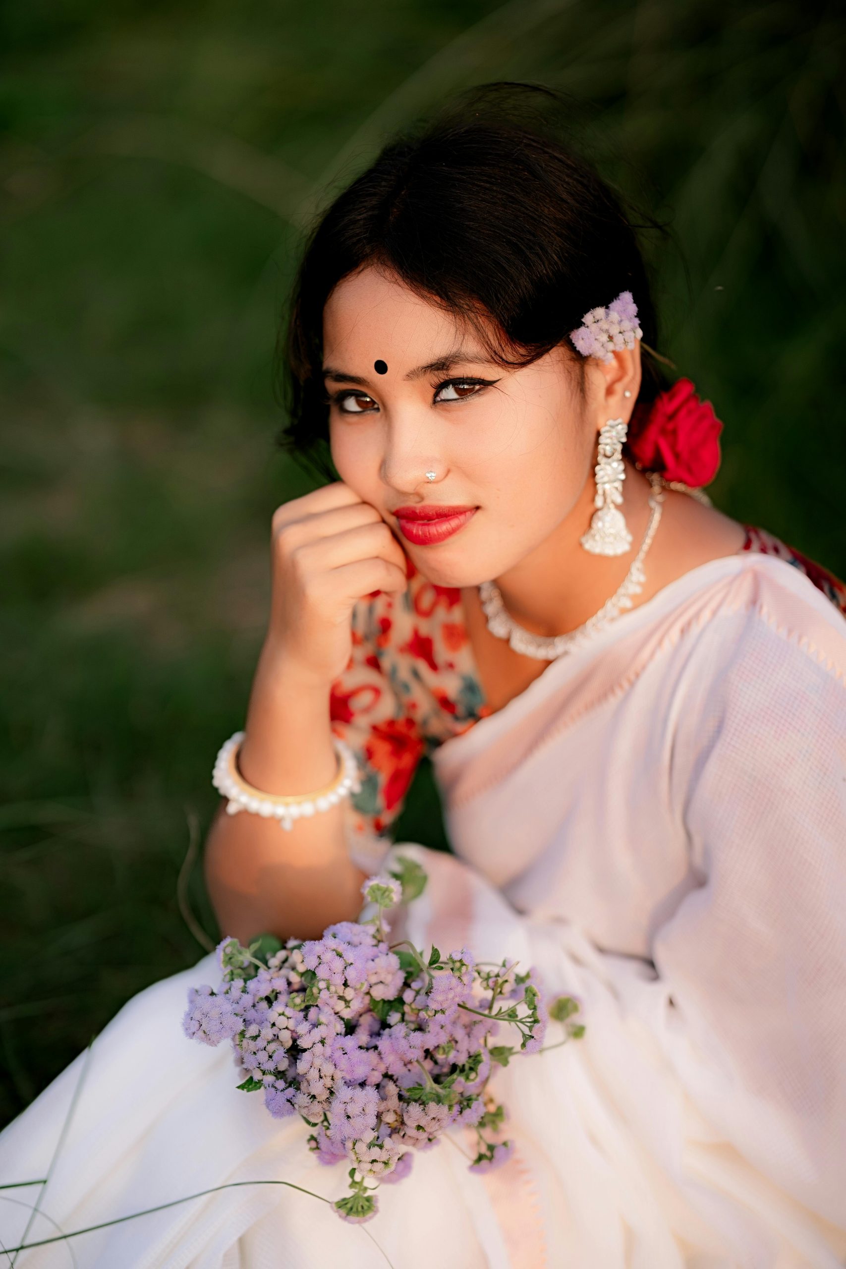 A beautiful Bangladeshi woman in traditional attire holding flowers outdoors.