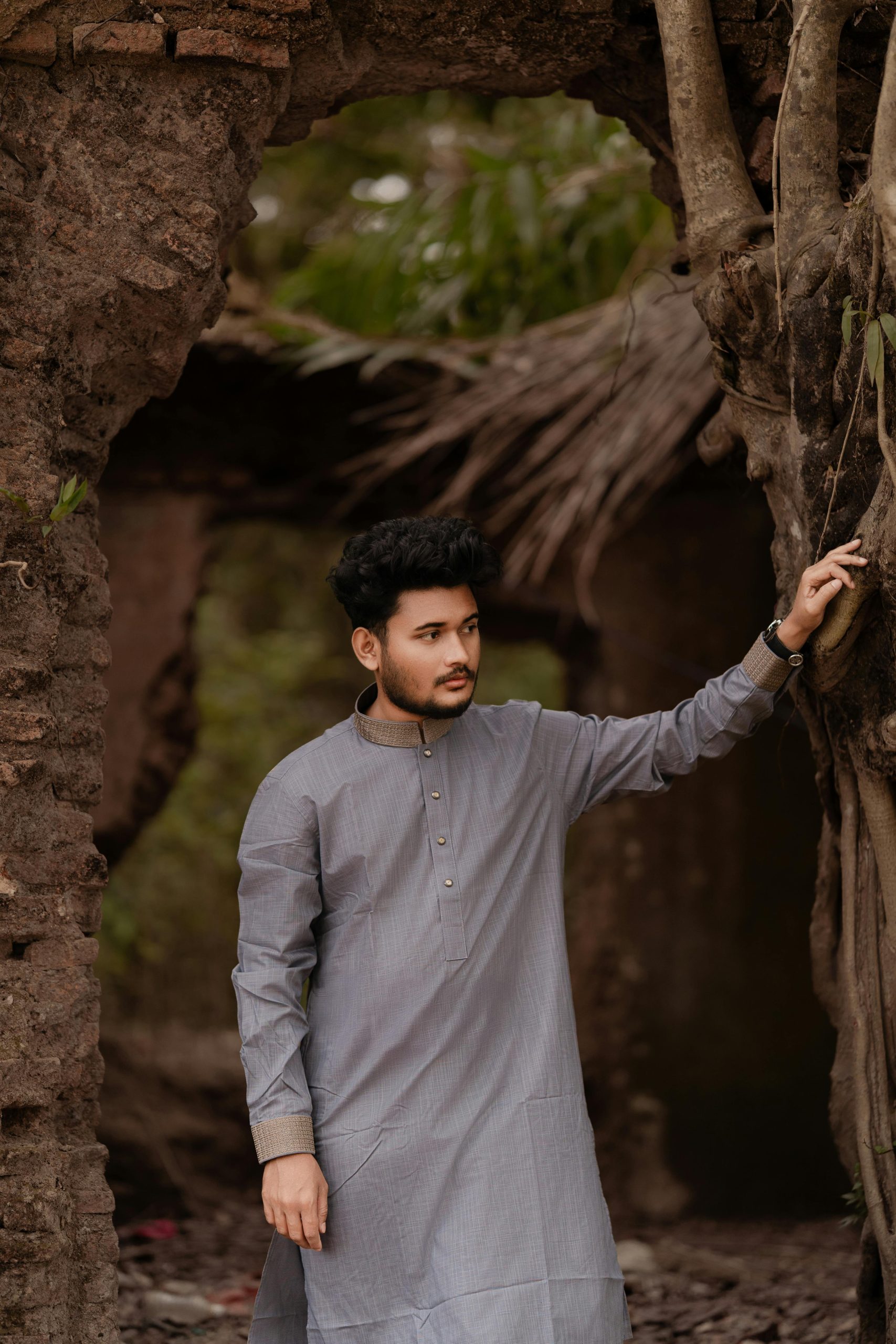 A young man in traditional Panjabi attire stands outdoors in rural Bangladesh.